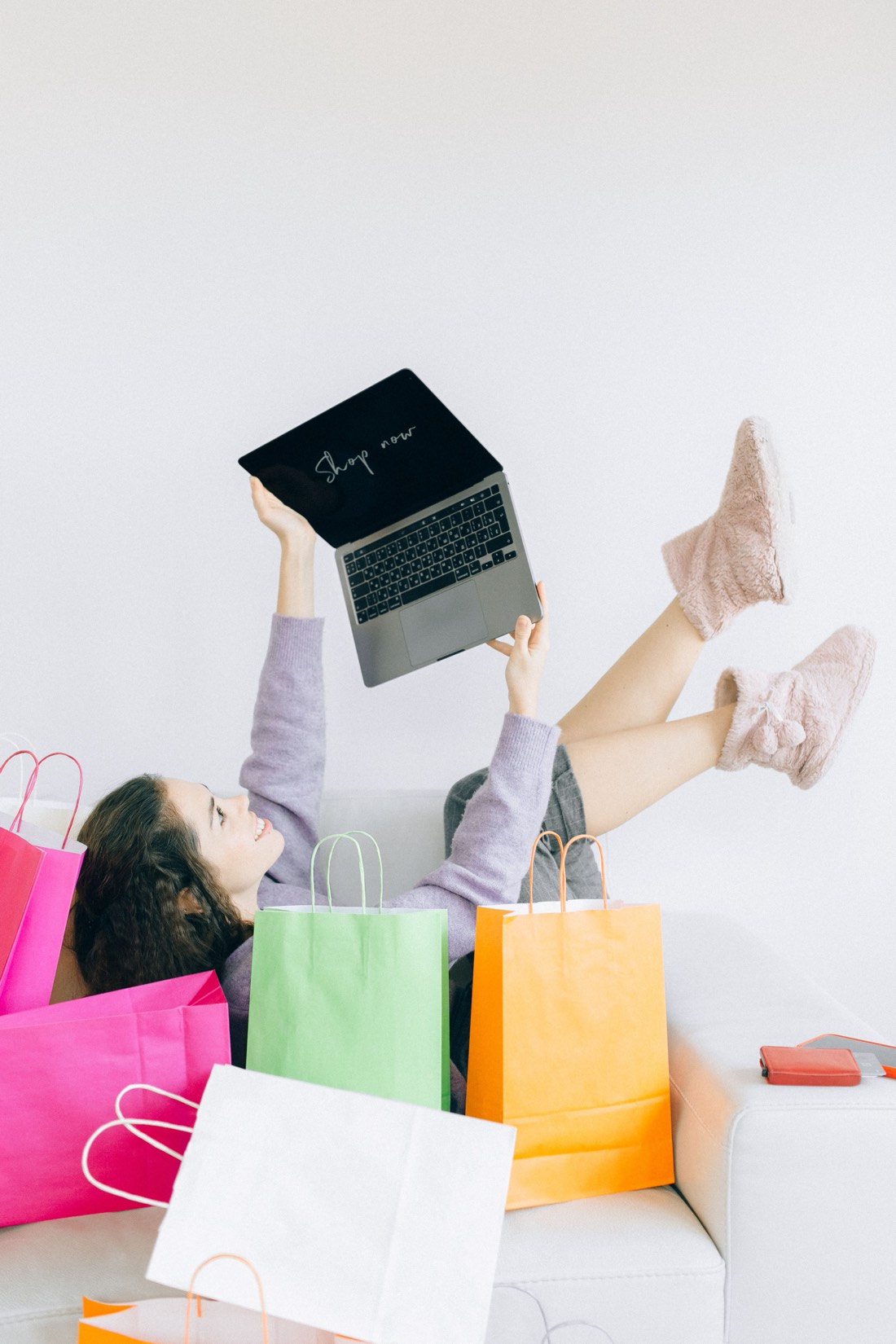 A happy shopper surrounded by colourful shopping bags, holding a laptop that says Shop now